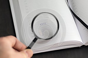 Open notebook with entry of word mute viewed through magnifying glass held in hand. Time of rest or quiet