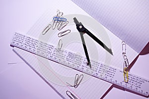An open notebook with paper clips, a ruler and a compass. Open notebook in a cage with school accessories. Office Chancellery.