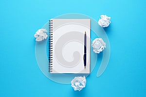 Open notebook, pen and crumpled paper balls on blue background.