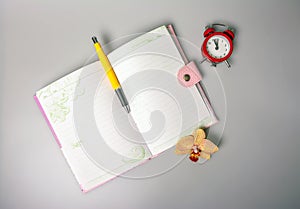 An open notebook, pen, orchid flower and an alarm clock reminiscent of time are on the table.