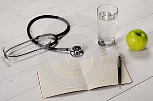 Open notebook with pen, stethoscope, apple and a glass water photo