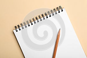 Open notebook and pencil on beige background, top view