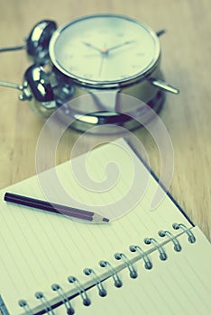 Open notebook with pencil and old-fashioned alarm clock on wood