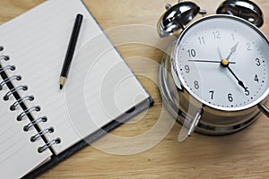 Open notebook with pencil and old-fashioned alarm clock on wood