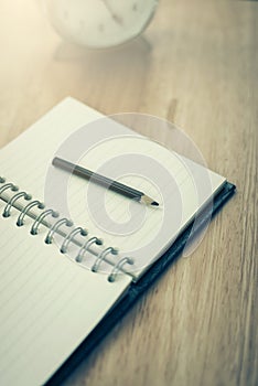 Open notebook with pencil and old-fashioned alarm clock on wood
