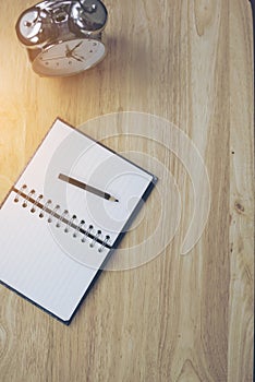 Open notebook with pencil and old-fashioned alarm clock on wood