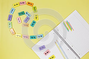 Open notebook, pencils and mathematical examples on yellow background. Back to school, fun learning of counting numbers for kids.