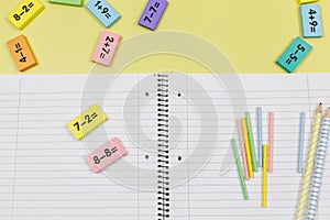 Open notebook, pencils and mathematical examples on yellow background. Back to school, fun learning of counting numbers for kids.