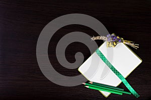 Open notebook with polka dot ribbon as a bookmark, boutonniere and green pencils.