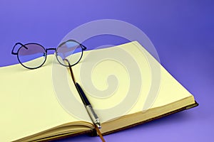 Open notebook and round glasses. Stylish glasses, notepad and pen, close-up. Blank pages of a notebook and glasses