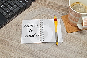 Open notebook with Spanish text `NUNCA TE RINDAS` Never Give Up and a cup of coffee on wooden background. photo