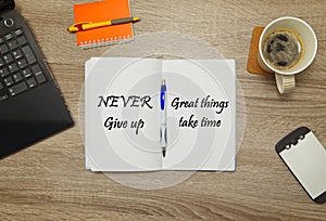 Open notebook with text `Never Give Up - great things take time` and a cup of coffee on wooden background.