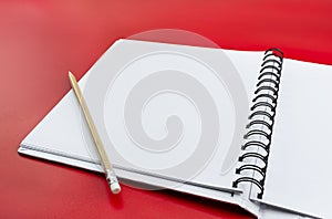 An open notebook with white pages and a wooden pencil lying on the left, isolated on a red background.