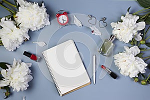 Open notebook for writing plans, to-do list or dreams with fresh peonies, alarm clock, cosmetics on light blue background