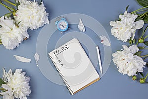 Open notebook for writing plans, to-do list or dreams with fresh peonies, alarm clock, on light blue background