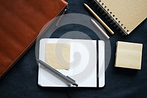 Open notepad with black pen next to laptop case, notepad and pens on dark background