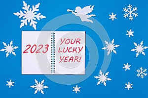 An open notepad diary with the Text 2023 and YOUR LUCKY YEAR on a blue background with Christmas snowflakes