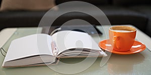Open notepad with pen in the middle, cup of coffee and digital tablet on coffee table
