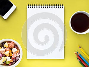 Open notepad on the spiral with a clean white page, a Cup with tea, caramels in a bowl, smartphone and crayon