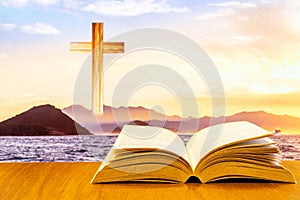 Open old bible on a wood table with blurred cross & colourful clouds and sky as background