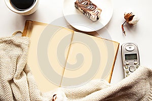 Open old book with empty pages, sweater, coffee cup and chocolate cake on white background.