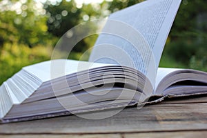 Open old book with flipping book pages on wooden table outdoors.