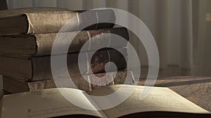 Open old book and pile of old books on a wooden table on sunrise light