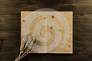 Open old vintage book on the aged wooden background. ears of wheat.