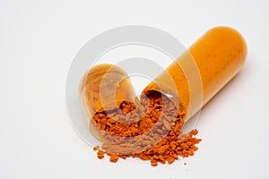 An open orange pill on a white background releases the orange powdery contents