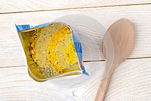 Open package with universal seasoning and wooden spoon on a white wooden table. Seasoning contains salt and dried vegetables.