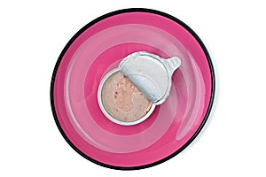 Open package of wet pet food on pink plate, seen directly from above.