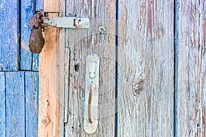 Open padlock on a scuffed wooden door with weathered cracks of blue and beige colors of old country house