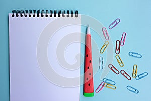 Open paper notebook with a red pen and colorful paper clips on blue background. Back to school concept.