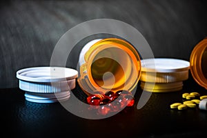 Open pill bottles on table top with red gel caps and yellow pills