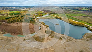 Open pit gravel mining site with lake or pond of unusual shape and beautiful autumn nature, gravel piles photographed with drone