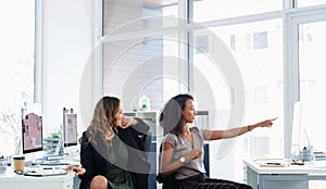 Open plan makes for open dialogue. two young businesswomen using a computer together in a modern office.