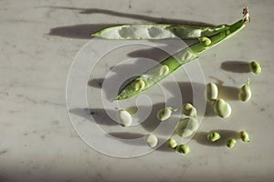 Open pod of broad beans and scattered beans on marble surface