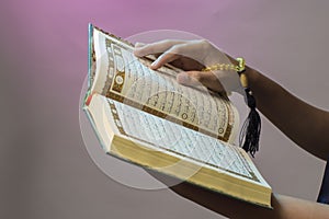 The open Qur& x27;an is held by the hand holding the prayer beads & x28;tasbih& x29;. The Qur& x27;an is the holy book of Islam