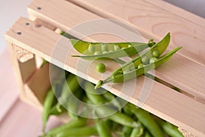 Open, raw, fresh pea pods and pea on wooden, brown box