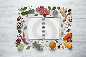 Open recipe book and ingredients on white wooden table, flat lay. Space for text