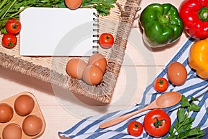 Open recipe book with fresh vegetables on wooden table.
