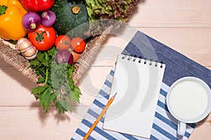 Open recipe book with fresh vegetables on wooden table.