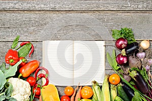 Open recipe book with set of raw organic vegetables on vintage wooden table