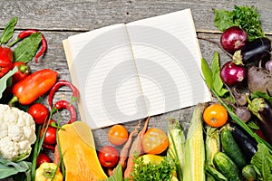 Open recipe book with set of raw organic vegetables on vintage wooden table