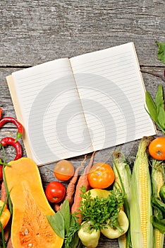 Open recipe book with set of raw organic vegetables on vintage wooden table