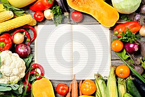 Open recipe book with set of raw organic vegetables on vintage wooden table