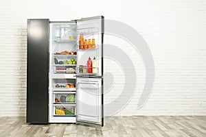 Open refrigerator filled with food near white brick wall, space for text