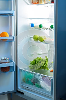 Open refrigerator full of food on kitchen