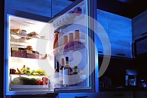 Open refrigerator full of products in kitchen