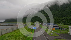 Open road and coastal houses by tunnel in forested fog covered mountain